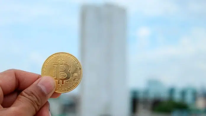Pessoa segurando moeda de Bitcoin ao ar livre.