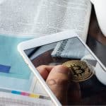 Figura de um Bitcoin em aplicativo, próximo de jornal