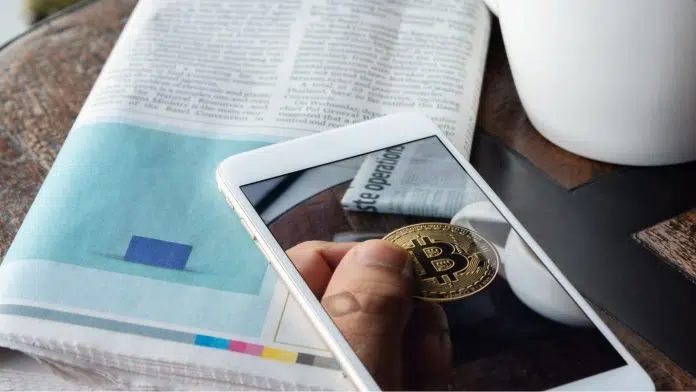 Figura de um Bitcoin em aplicativo, próximo de jornal