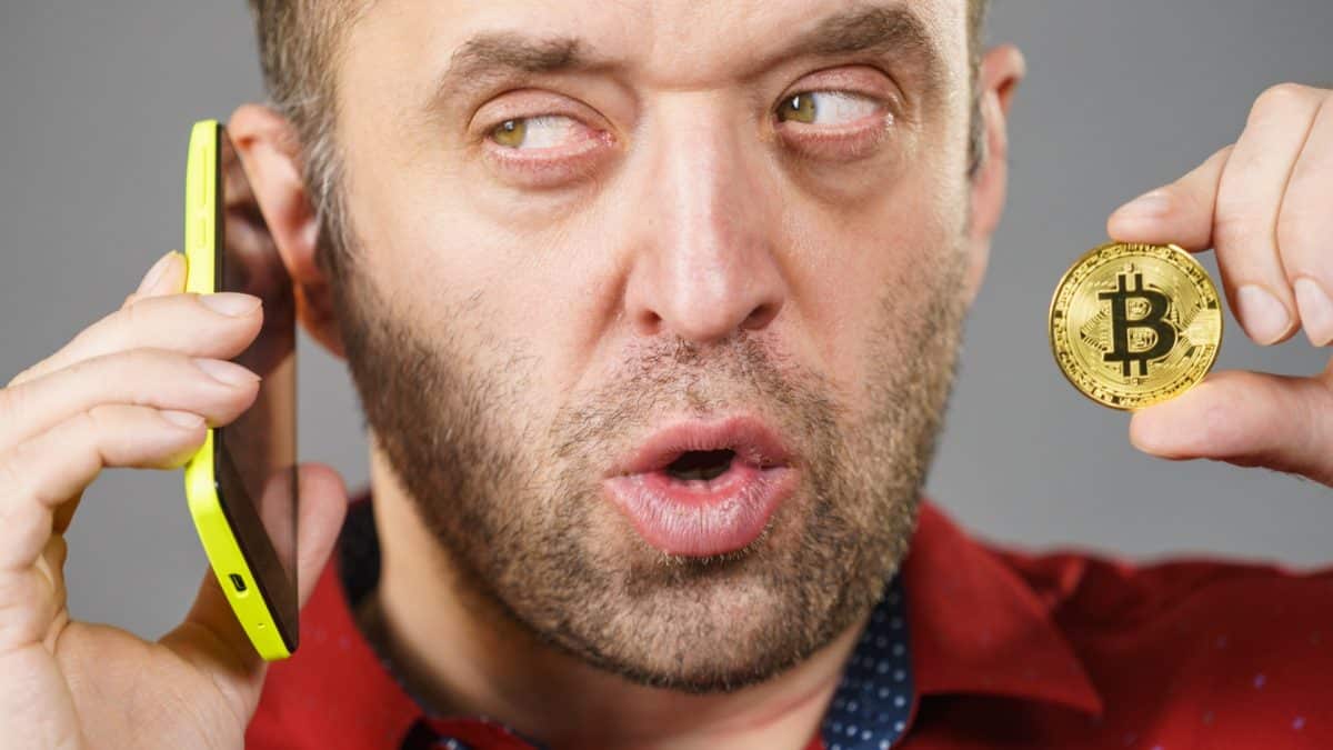 Homem com olhar suspeito em conversa pelo telefone e segurando Bitcoin