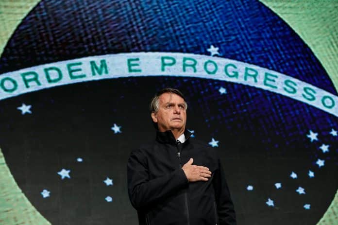 Presidente Jair Bolsonaro com bandeira do Brasil ao fundo