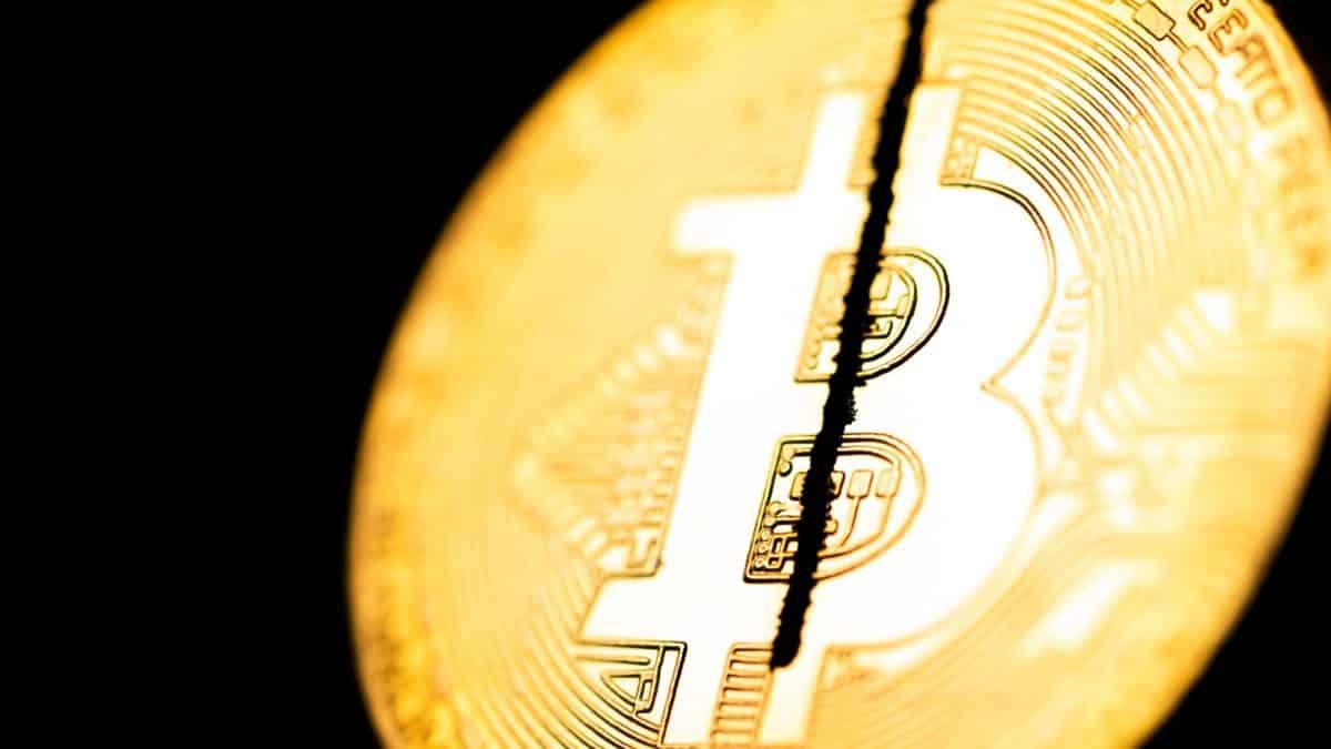 Moeda física de Bitcoin sendo cortada ao meio.