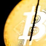 Moeda física de Bitcoin sendo cortada ao meio.