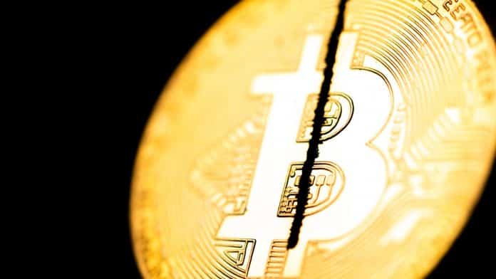 Moeda física de Bitcoin sendo cortada ao meio.