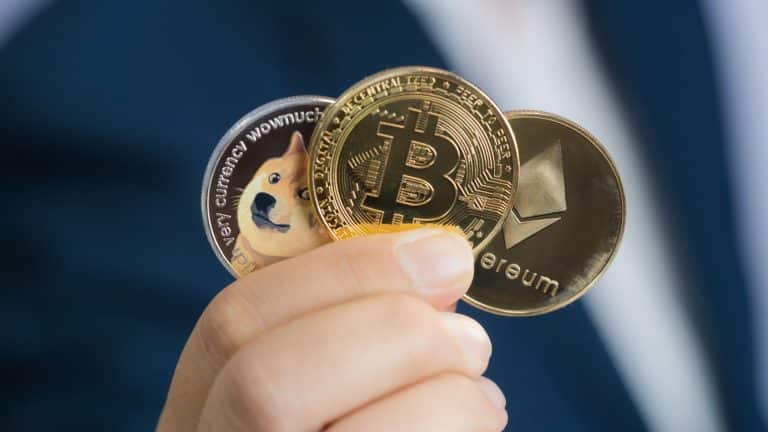 Investidor segurando moedas físicas de Dogecoin, Bitcoin e Ethereum.