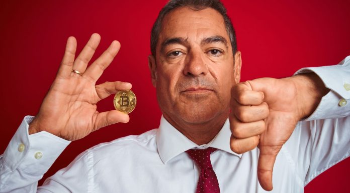 Homem segurando moeda de Bitcoin e fazendo sinal de negativo com a outra.