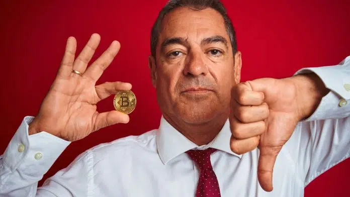Homem segurando moeda de Bitcoin e fazendo sinal de negativo com a outra.