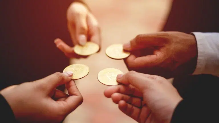 Grupo de pessoas segurando moedas físicas de Bitcoin.