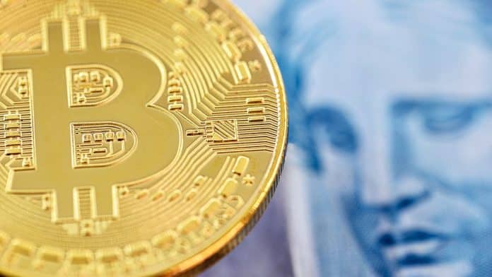 Bitcoin ao lado de nota de Real brasileiro, moeda emitida pelo Banco Central do Brasil