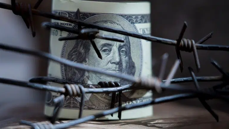 Dinheiro do dólar americano envolto em arame farpado como símbolo de guerra econômica, sanções e embargo