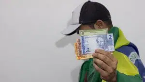 Homem com bandeira do Brasil segurando título de eleitor próximo de notas