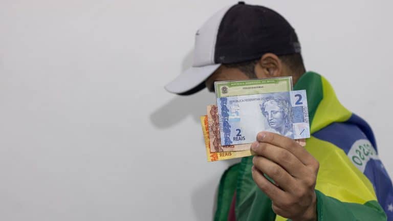 Homem com bandeira do Brasil segurando título de eleitor próximo de notas