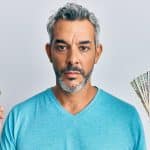 Homem sério segurando bitcoin e notas de dinheiro