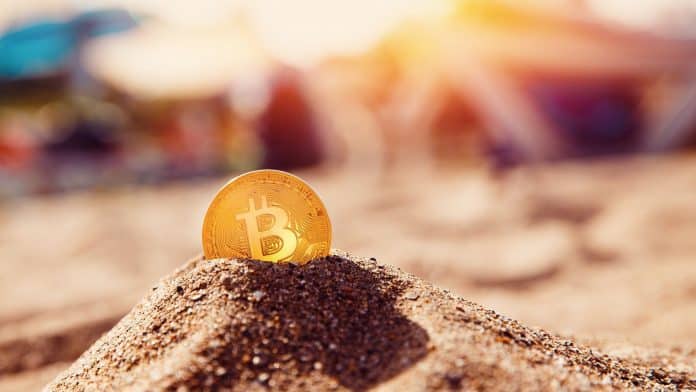 Moeda bitcoin enterrada em areia da praia