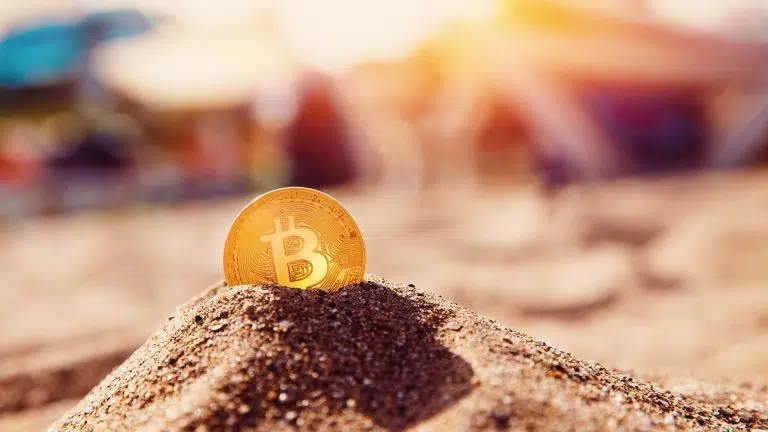 Moeda bitcoin enterrada em areia da praia