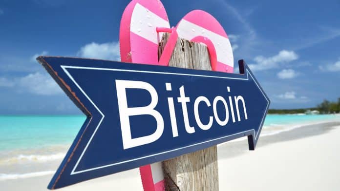 Placa com escrita de Bitcoin apontando para praia