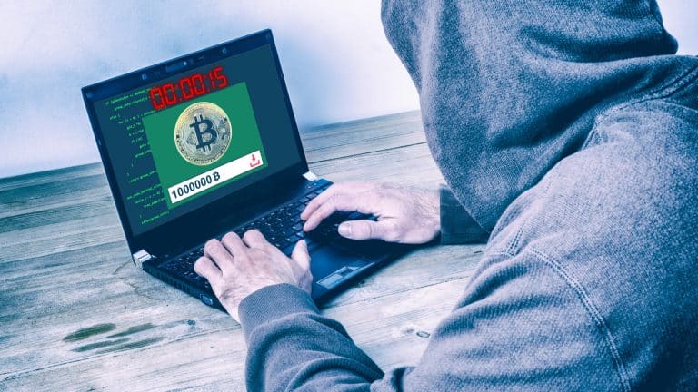 Visão traseira de um hacker vestindo um capuz e roubando bitcoins em uma tela de laptop e criptomoedas