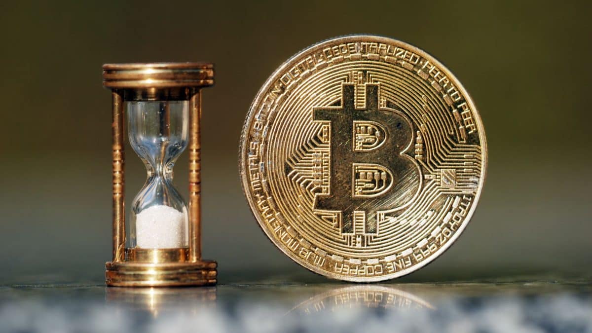 Moeda física de Bitcoin ao lado de ampulheta.
