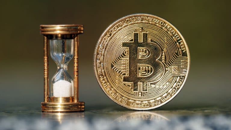 Moeda física de Bitcoin ao lado de ampulheta.