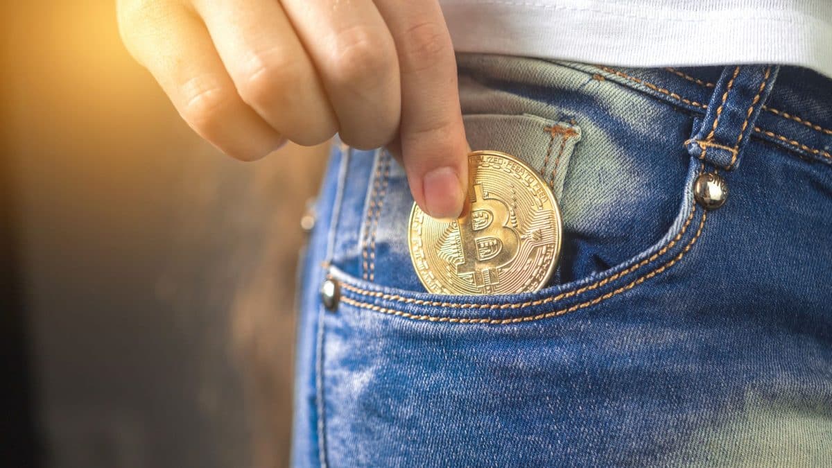 Investidor guardando moeda física de Bitcoin em seu bolso.