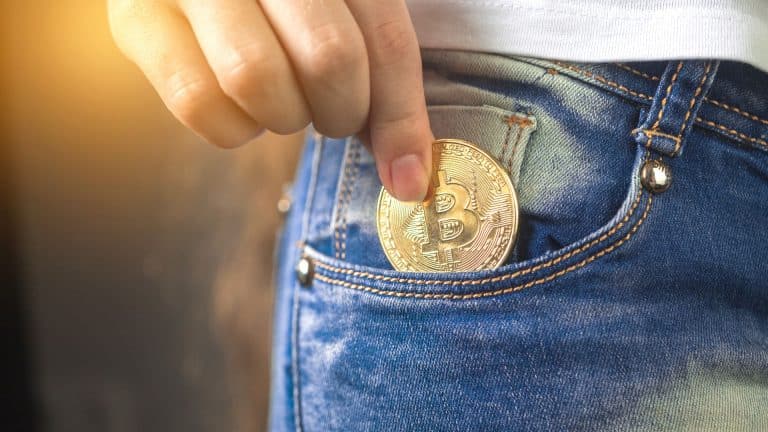 Investidor guardando moeda física de Bitcoin em seu bolso.