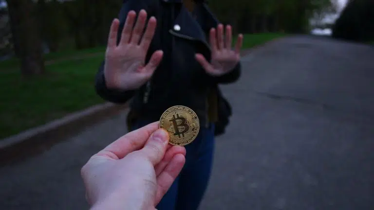 Pessoa recusando bitcoin em versão física, símbolo