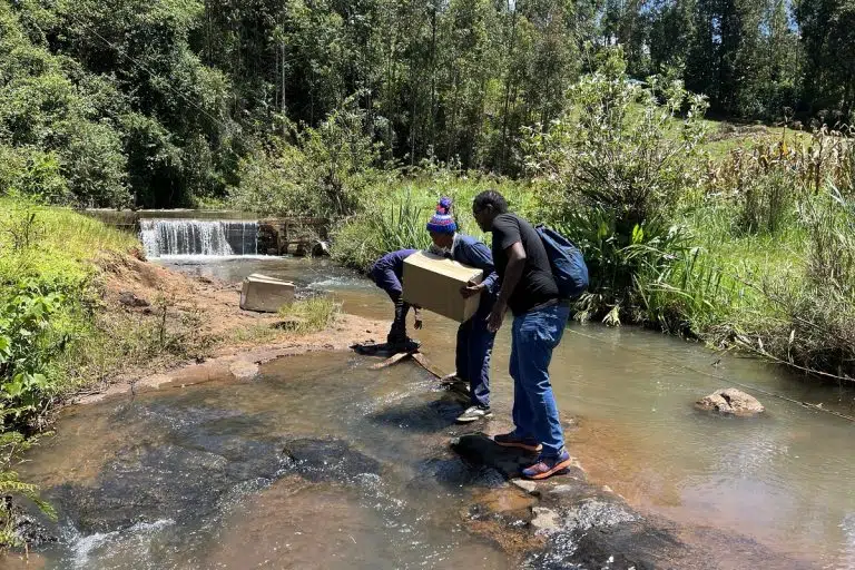 Homens carregando equipamentos para montar estrutura de mineração de bitcoin em zona rural do Quênia