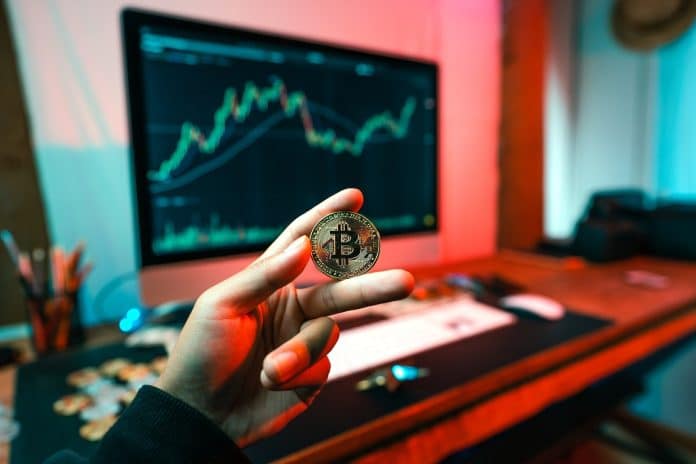 Bitcoin entre dedos com fundo vermelho de queda, desvalorização
