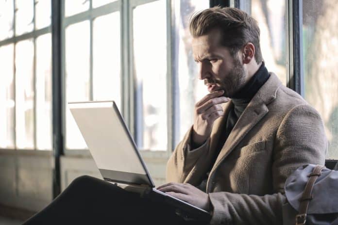 Homem em dúvida ao trabalhar em computador corretora problema de criptomoedas