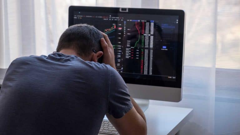 Investidor desolado em frente a computador com site de corretora de criptomoedas.