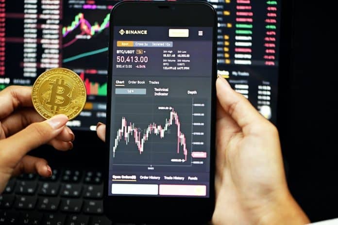 Aplicativo e site da Binance ao lado de bitcoin. Foto Kanchanara.