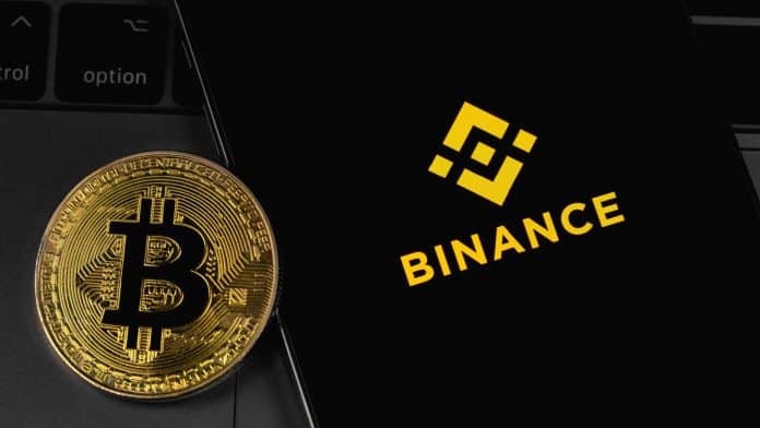 Moeda de Bitcoin ao lado de app da Binance.