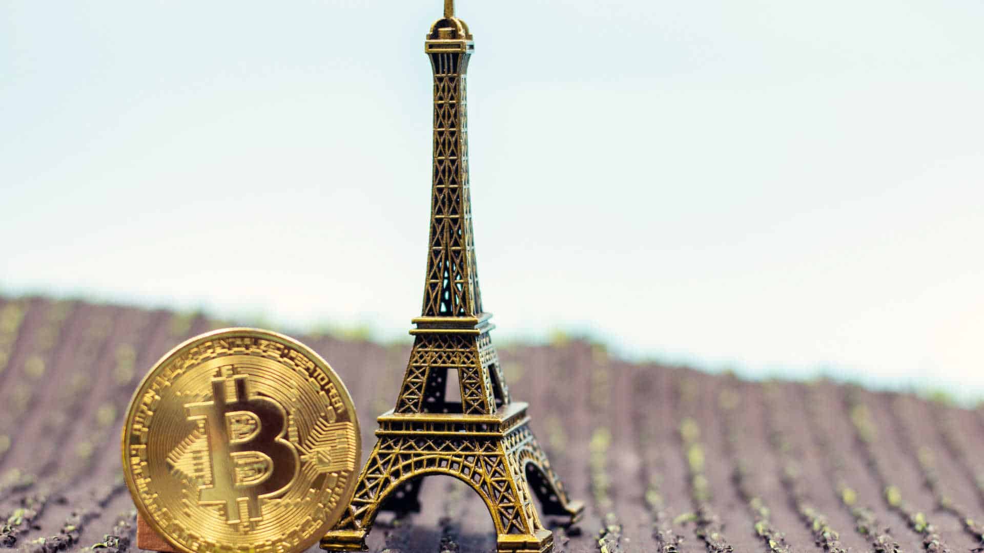 Moeda de Bitcoin ao lado de torre Eiffel.