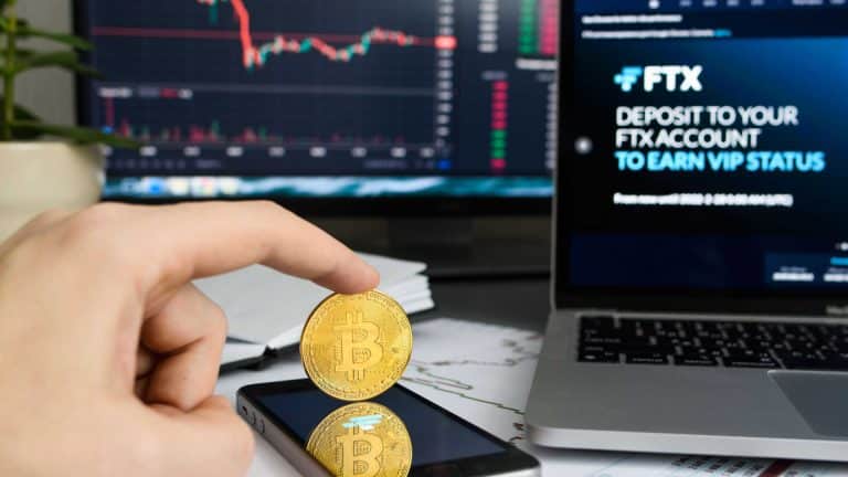 Investidor segurando moeda de Bitcoin ao lado de site da FTX.