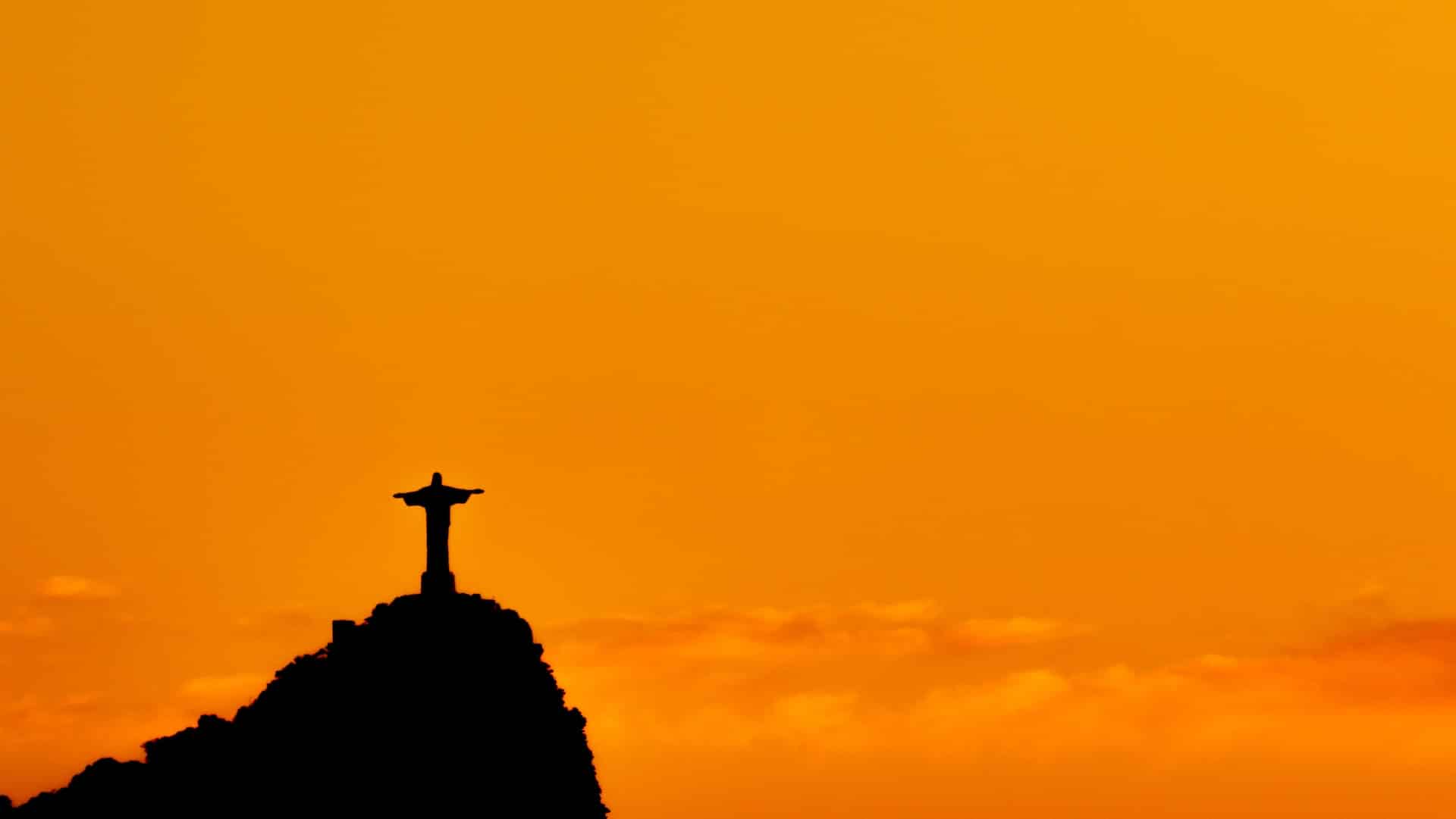 Cristo Redentor em destaque com céu laranja