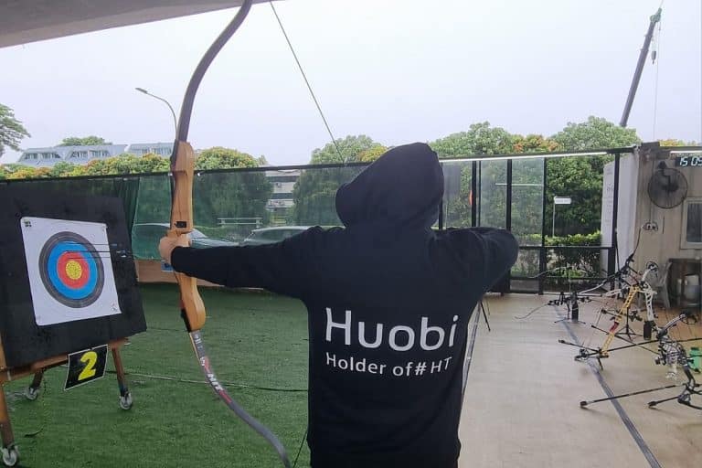 Homem com arco e flecha vestindo blusa da corretora de criptomoedas Huobi