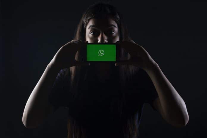 Mulher com segurando telefone com WhatsApp aberto em destaque