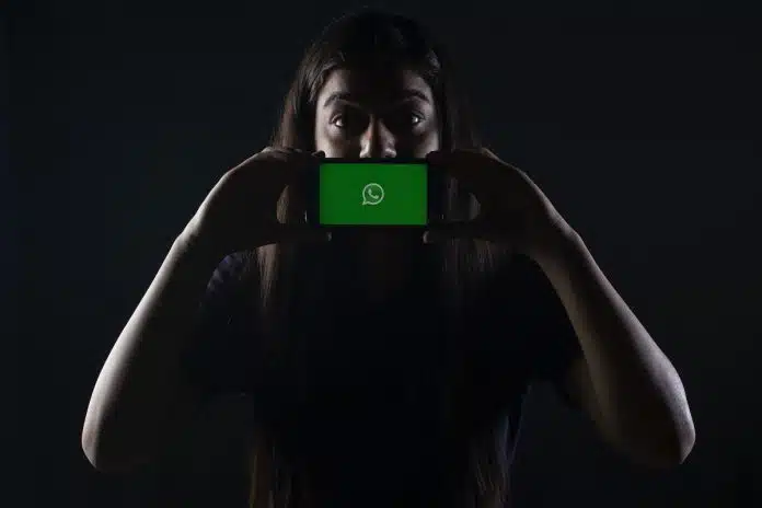 Mulher com segurando telefone com WhatsApp aberto em destaque