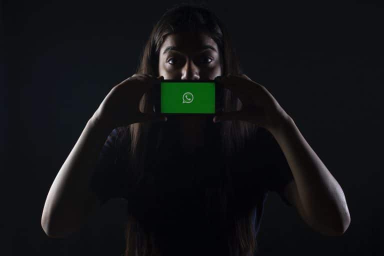 Mulher com segurando telefone com WhatsApp aberto em destaque