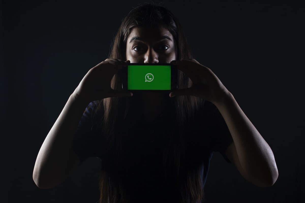 Mulher com segurando telefone com WhatsApp aberto em destaque