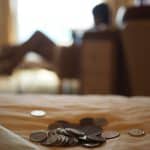 Mulher no sofá ao fundo, moedas sobre a mesa na frente