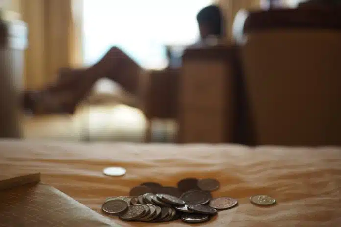 Mulher no sofá ao fundo, moedas sobre a mesa na frente