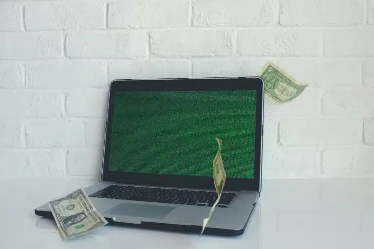 Computador com tela hackeada com notas de dólares voando ao lado