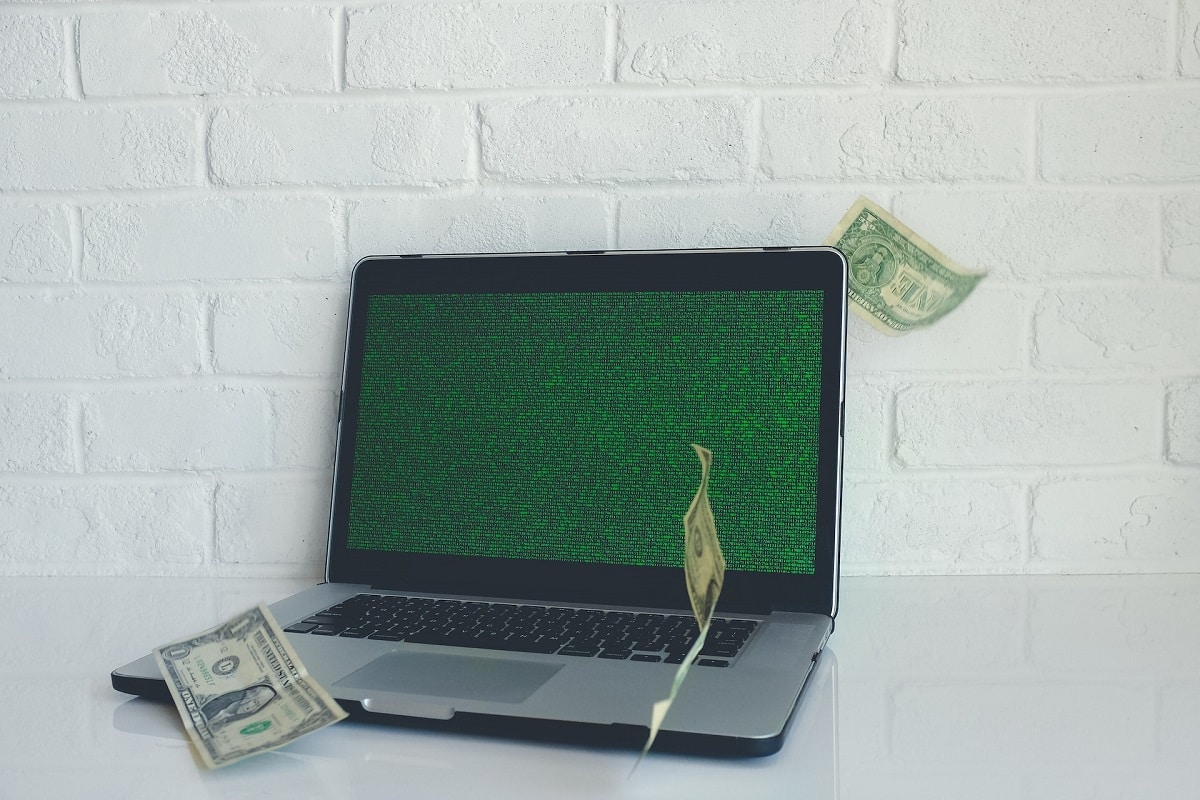 Computador com tela hackeada com notas de dólares voando ao lado