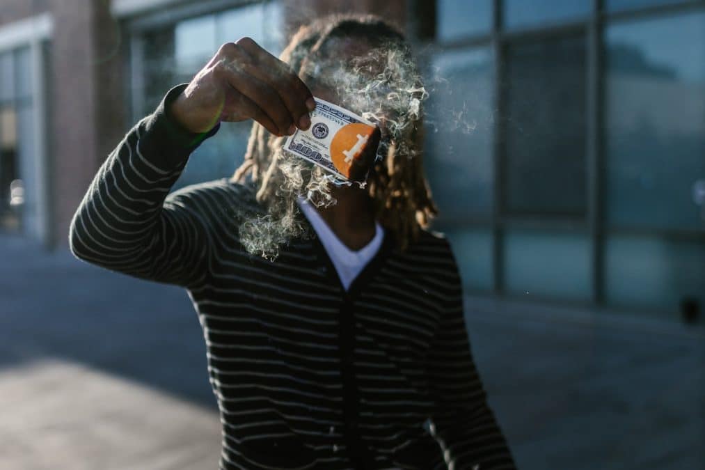 Homem segurando nota pegando fogo com símbolo do bitcoin