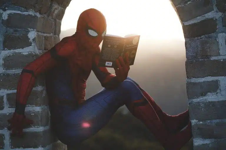 Homem vestido de Homem Aranha segurando livro enquanto escala prédio