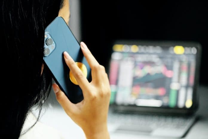 Pessoa falando em telefone com notebook mostrando gráficos de investimentos
