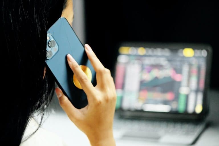 Pessoa falando em telefone com notebook mostrando gráficos de investimentos