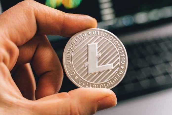 Mão segurando Litecoin simbólico com gráficos ao fundo alta