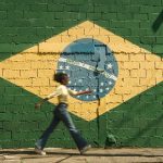 Mulher passando em frente a bandeira do Brasil pintada em muro